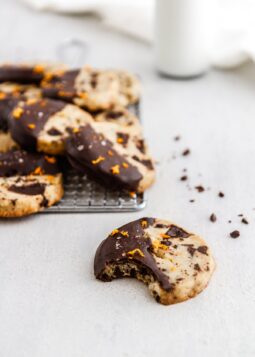 a chocolate orange shortbread cookie with a bite out of it and more cookies in the background